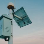 A solar panel paired with a security camera against a clear sky, representing renewable technology.