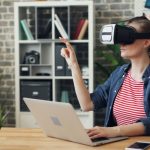 A woman using a VR headset while working on a laptop, exploring virtual reality in a modern office setting.